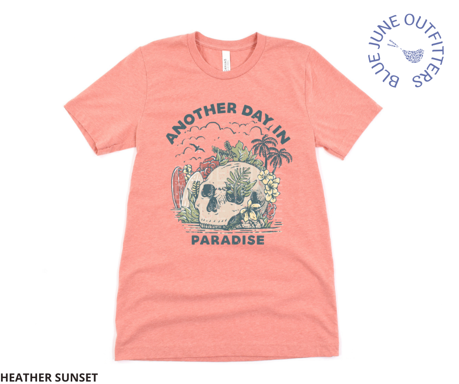 Super soft Bella + Canvas shirt in heather clay. This tee is features a skull on the beach with palm trees, surf boards and seagulls with the text another day in paradise. This is from Blue June Outfitters' exclusive Morbid Nature Collection.