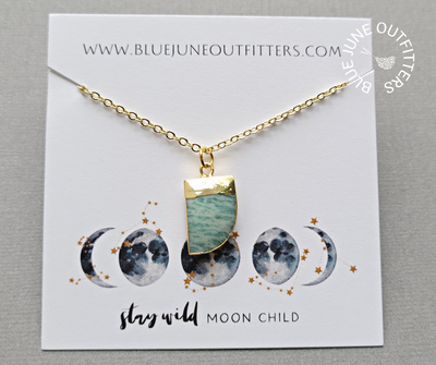 Gold plated necklace with electroplated amazonite gemstone pendant, shaped as a horn and electroplated. Displayed here on a jewelry card with our website at the top and a blue and gold moon phase at the bottom that reads STAY WILD MOON CHILD. The necklace is thoughtfully packaged and ready for gifting.