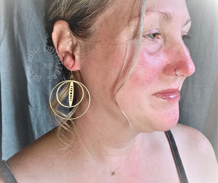 Model profile wearing a pair of the moon phase earrings with 2 circle pendants. They are made of raw brass and are gold in color. Bohemian chic. 