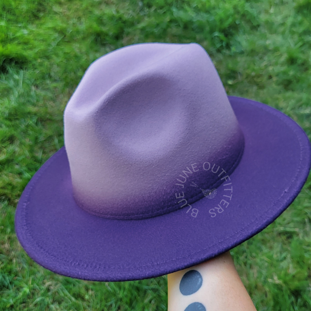 Purple hat held by a hand against a grassy background
