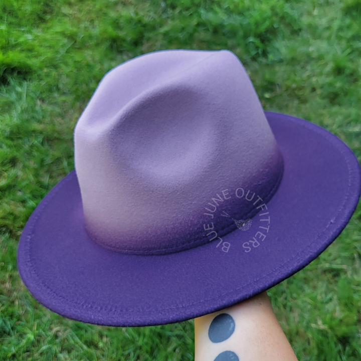 Purple hat held by a hand against a grassy background