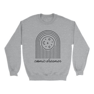 Sport grey unisex crewneck sweatshirt against a white background. The image on the sweatshirt is of stars and moons. In cursive, the text reads cosmic dreamer.