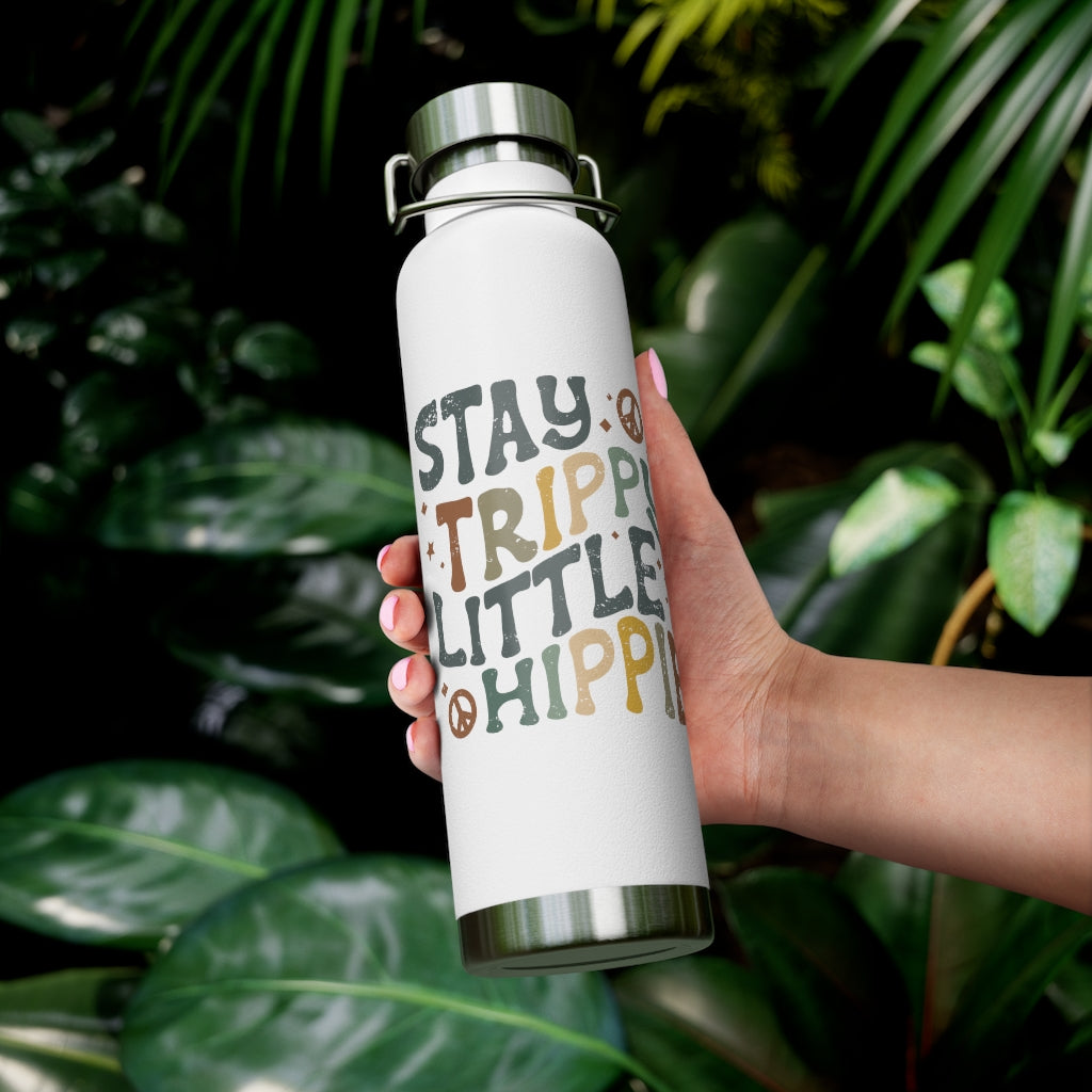 Clear view of the bottle with the artwork being held in one hand in front of tropical foliage. 