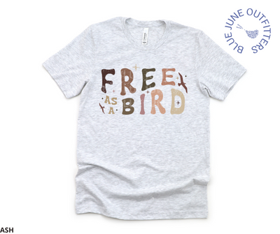 Unisex Bella + Canvas brand tee in ash grey. This shirt is from Blue June Outfitters exclusive Hippie Collection The shirt reads Free As A Bird. It is a trippy retro font in earthy colors. There are small birds in flight and stars around the text.
