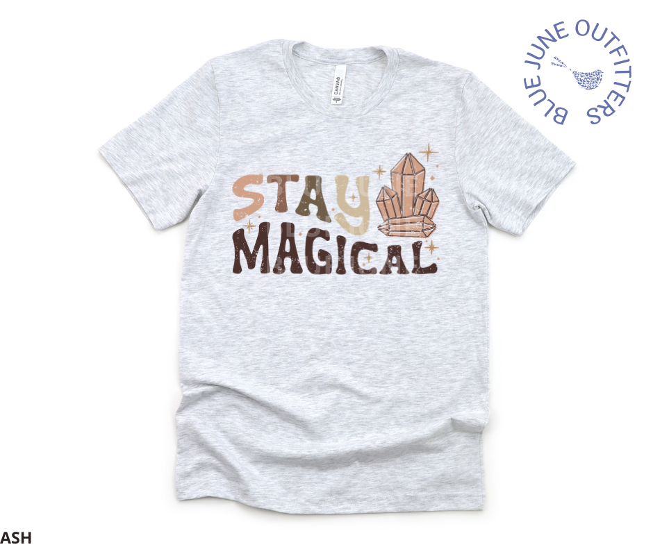 Bella + Canvas brand unisex tee in ash grey. Shown here laid flat on a solid white surface. This shirt is from Blue June Outfitters' exclusive Hippie Collection. It features small stars and healing crystals. The text is retro with earthy colors and reads Stay Magical.