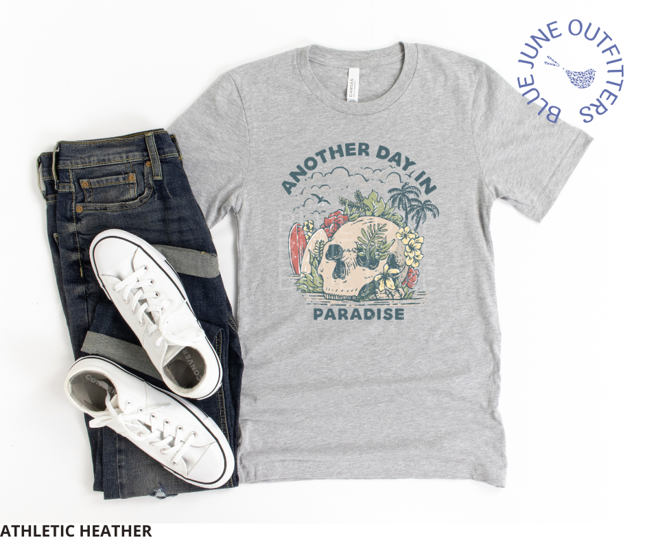Super soft Bella + Canvas shirt in athletic heather shown paired with a pair of dark blue jeans. This tee is features a skull on the beach with palm trees, surf boards and seagulls with the text another day in paradise. This is from Blue June Outfitters' exclusive Morbid Nature Collection.
