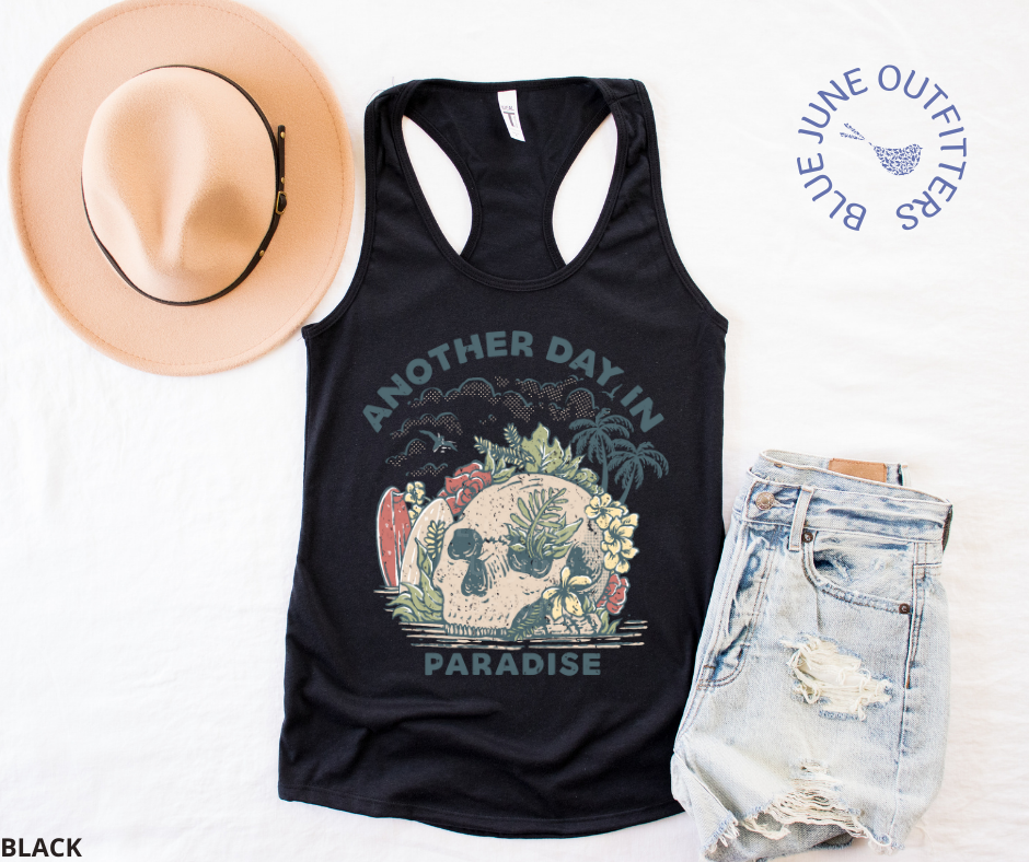Super soft women's slim fit racerback tank top in black. Paired here with jean shorts and a trendy hat. This tank is from Blue June Outfitters' exclusive Morbid Nature Collection and features a skull on the beach with palm trees, tropical plants, seagulls and surf boards. The text reads another day in paradise.