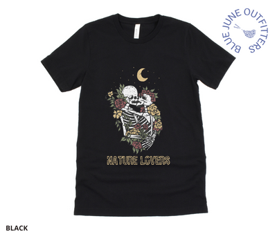 Super soft Bella + Canvas brand tee in black. This shirt from Blue June Outfitters' exclusive Morbid Nature Collection features two skeletons in a loving embrace wrapped in nature under the crescent moon that reads nature lovers at the bottom. This is our take on the lovers tarot card.