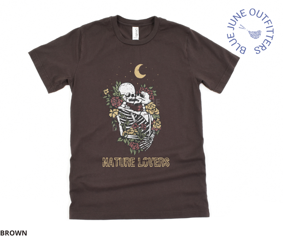 Super soft Bella + Canvas brand tee in brown. This shirt from Blue June Outfitters' exclusive Morbid Nature Collection features two skeletons in a loving embrace wrapped in nature under the crescent moon that reads nature lovers at the bottom. This is our take on the lovers tarot card.