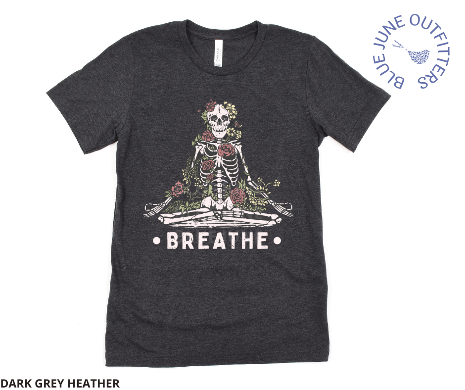 Super soft Bella + Canvas brand tee in dark grey heather. A tee from Blue June Outfitters' exclusive Morbid Nature collection with a meditating skeleton surrounded by wildflowers and the phrase breathe printed underneath.