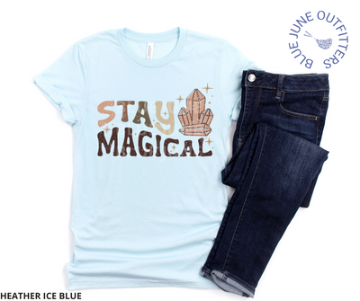 Bella + Canvas brand unisex tee in heather ice blue. Shown here with a pair of dark blue jeans. This shirt is from Blue June Outfitters' exclusive  Hippie Collection. It features small stars and healing crystals. The text is retro with earthy colors and reads Stay Magical.