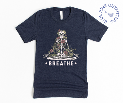 Super soft Bella + Canvas brand tee in heather midnight navy. A tee from Blue June Outfitters' exclusive Morbid Nature collection with a meditating skeleton surrounded by wildflowers and the phrase breathe printed underneath.