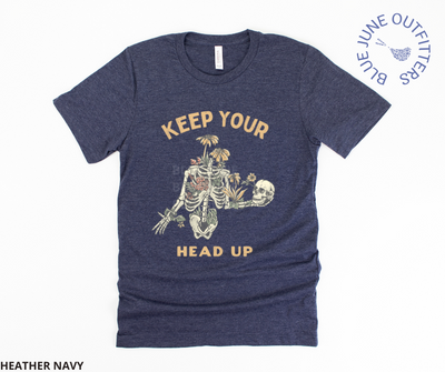 Super soft Bella + Canvas tee in heather navy. This shirt from Blue June Outfitters' exclusive Morbid Nature Collection features a skeleton covered in plants holding his skull up in his hands with the phrase keep your head up. This is the perfect tee for those who share