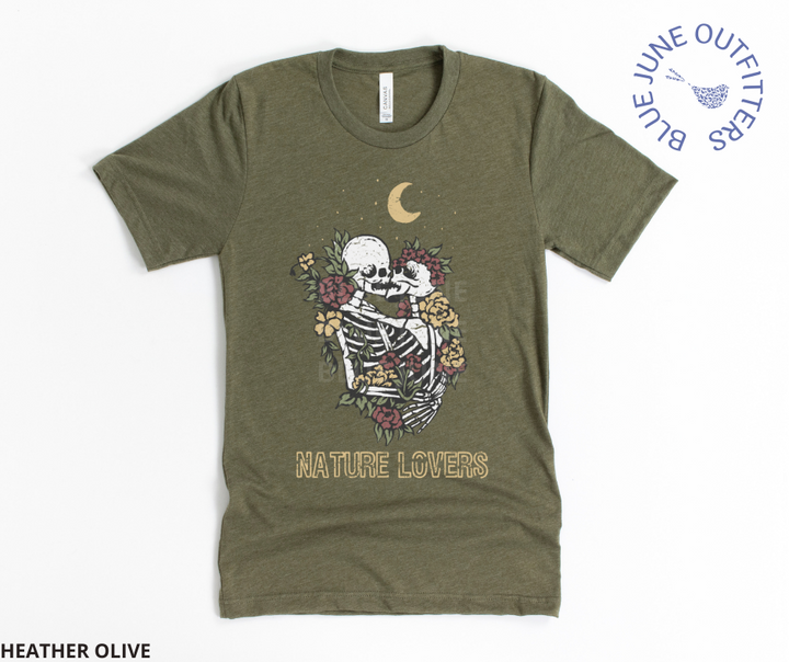 Super soft Bella + Canvas brand tee in heather olive. This shirt from Blue June Outfitters' exclusive Morbid Nature Collection features two skeletons in a loving embrace wrapped in nature under the crescent moon that reads nature lovers at the bottom. This is our take on the lovers tarot card.