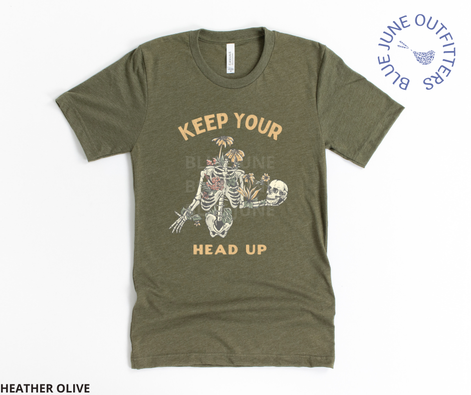 Super soft Bella + Canvas tee in heather olive. This shirt from Blue June Outfitters' exclusive Morbid Nature Collection features a skeleton covered in plants holding his skull up in his hands with the phrase keep your head up. This is the perfect tee for those who share
