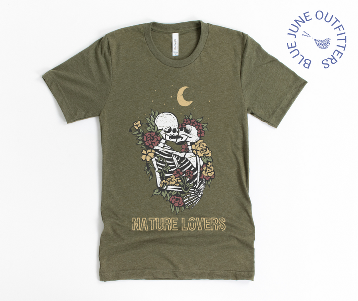 Super soft Bella + Canvas brand tee in heather olive. This shirt from Blue June Outfitters' exclusive Morbid Nature Collection features two skeletons in a loving embrace wrapped in nature under the crescent moon that reads nature lovers at the bottom. This is our take on the lovers tarot card.