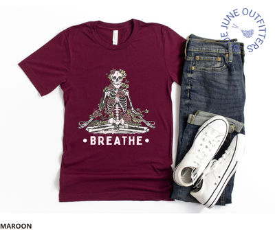 Super soft Bella + Canvas brand tee in maroon. A tee from Blue June Outfitters' exclusive Morbid Nature collection with a meditating skeleton surrounded by wildflowers and the phrase breathe printed underneath.