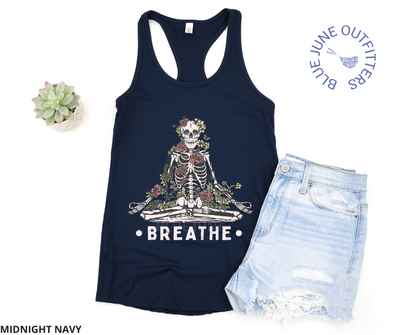 Super soft women's slim fit racerback tank top in midnight navy. This tank is from Blue June Outfitters' exclusive Morbid Nature Collection, featuring a skeleton practicing meditation covered in plants and wildflowers. The text underneath says breathe. Shown here with a pair of jean shorts.