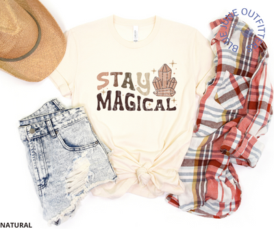 Bella + Canvas brand unisex tee in natural. Shown here with a flannel shirt, jean shorts and trendy hat. This shirt is from Blue June Outfitters' exclusive Hippie Collection. It features small stars and healing crystals. The text is retro with earthy colors and reads Stay Magical.