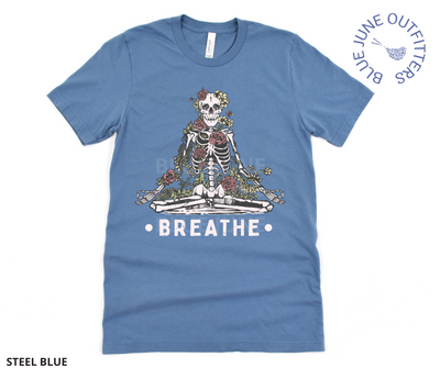 Super soft Bella + Canvas brand tee in steel blue. A tee from Blue June Outfitters' exclusive Morbid Nature collection with a meditating skeleton surrounded by wildflowers and the phrase breathe printed underneath.