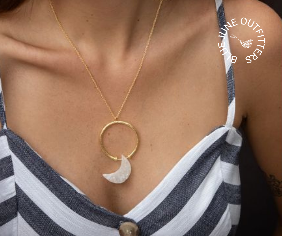 Bust of a female wearing a navy and white striped top and modeling the crescent moon druzy necklace. The pendant sits on a dainty gold chain. The pendent is a round gold ring, the druzy moon is white and drilled at the top to connect to the bottom of the ring. 