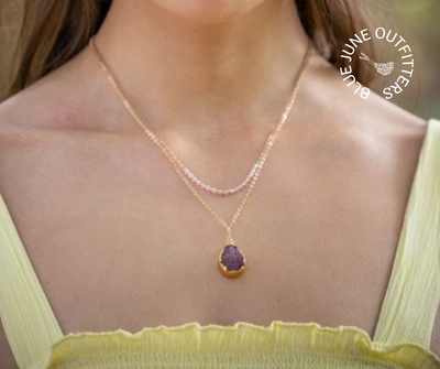 Female model in a yellow tank top wearing the layering necklace. The shortest layer falls just below her collar bone. The longer layer with the maroon druzy pendant falls just about an inch below that. 