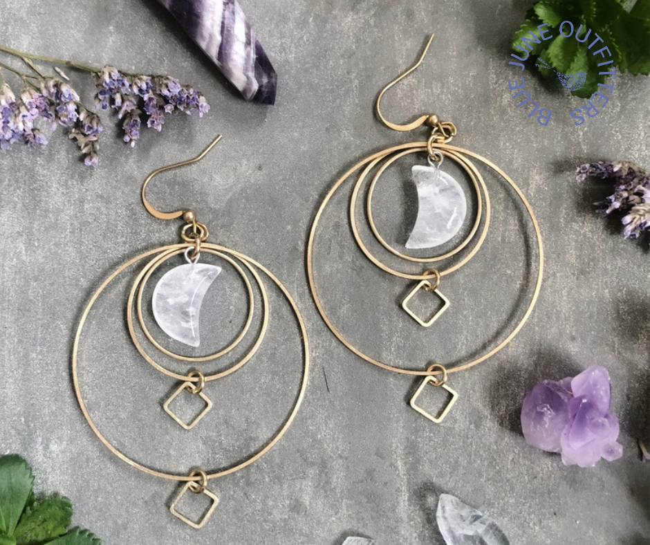 Pair of  gypsy style brass dangle earrings, each with clear quartz crystals shaped like crescent moons. There are three brass circles of different diameters and two small diamond shaped brass dangles. The brass ear hooks are hypo allergenic. 
