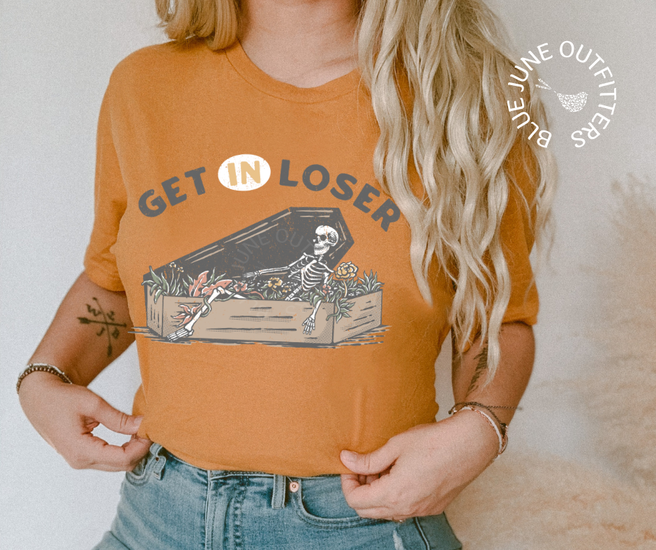 A mustard yellow unisex tee from Blue June Outfitters' Morbid Nature collection. Get In Loser with Skeleton and a coffin. Perfect for those who share our dark sense of humor.