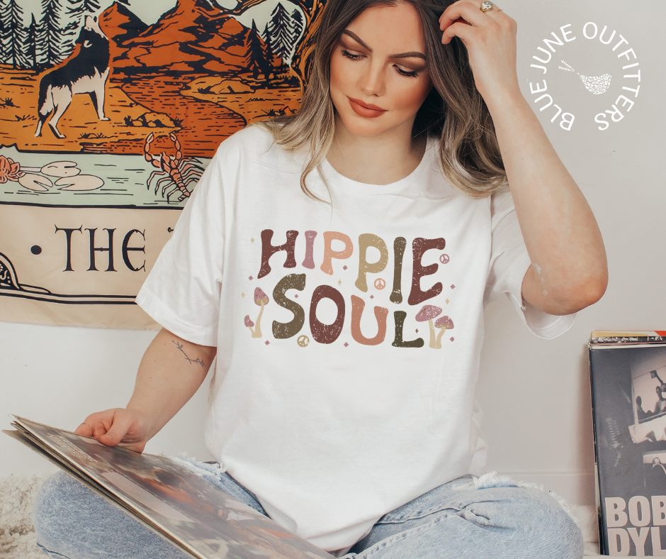 Female wearing the white bella canvas tee. This shirt is from Blue June Outfitters exclusive Hippie Collection. It features earthy wild mushrooms and small peace signs and reads hippie soul. Hippie Soul in written in a retro wavy font with earth tones. 