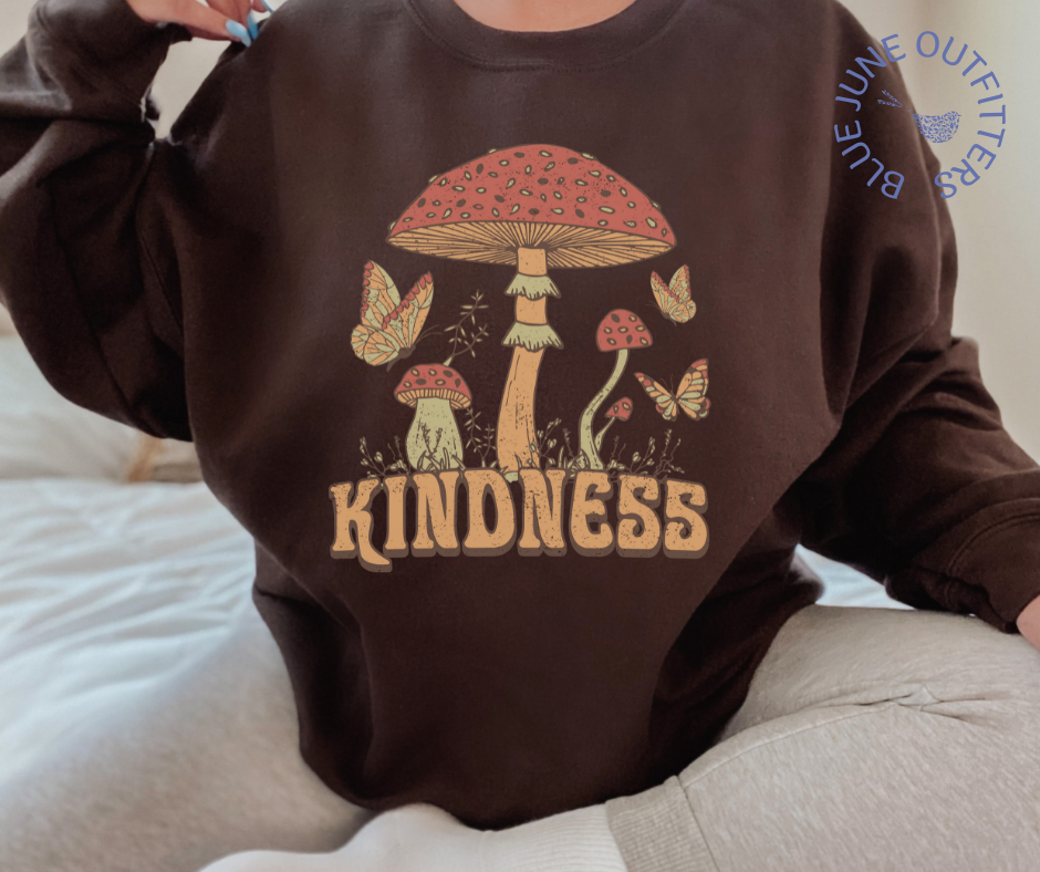 Model wearing the brown sweatshirt. The text reads KINDNESS. The artwork is vintage 1970's style mushrooms, plants and butterflies.