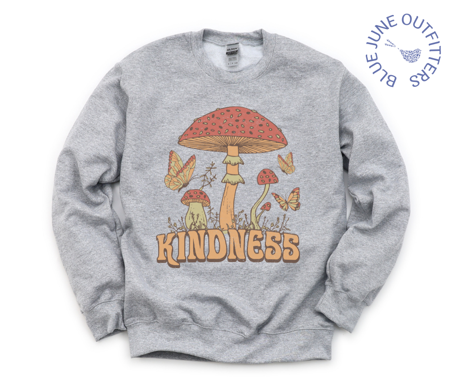 The sport grey sweatshirt lying flat on a solid white surface. The text reads KINDNESS. The artwork is vintage 1970's style mushrooms, plants and butterflies.