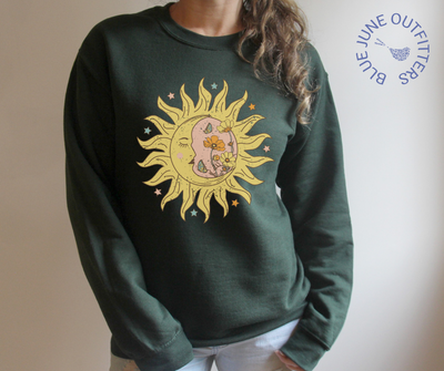 Model wearing the forest green unisex crewneck sweatshirt. The artwork printed is a bohemian sun and moon in one with vintage style flowers, stars and butterflies.