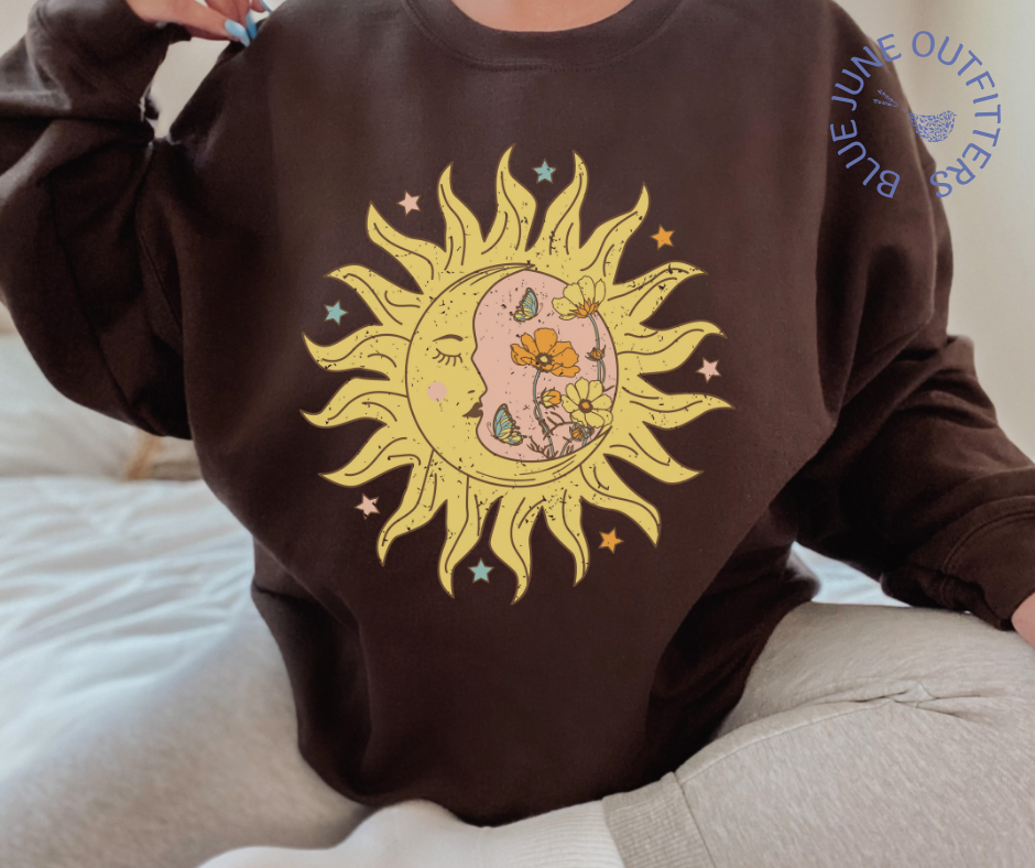 Model wearing the brown unisex crewneck sweatshirt. The artwork printed is a bohemian sun and moon in one with vintage style flowers, stars and butterflies.