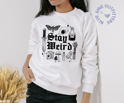 Female modeling the white sweatshirt. Artwork is black. It says stay weird. Surrounding the text are witchy things such as sage, stardust, mushrooms, skull, death potion, dagger, crystals and potions.