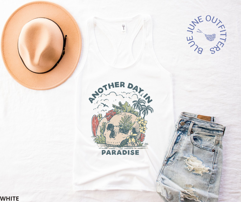 Super soft women's slim fit racerback tank top in white. Paired here with jean shorts and a trendy hat. This tank is from Blue June Outfitters' exclusive Morbid Nature Collection and features a skull on the beach with palm trees, tropical plants, seagulls and surf boards. The text reads another day in paradise.