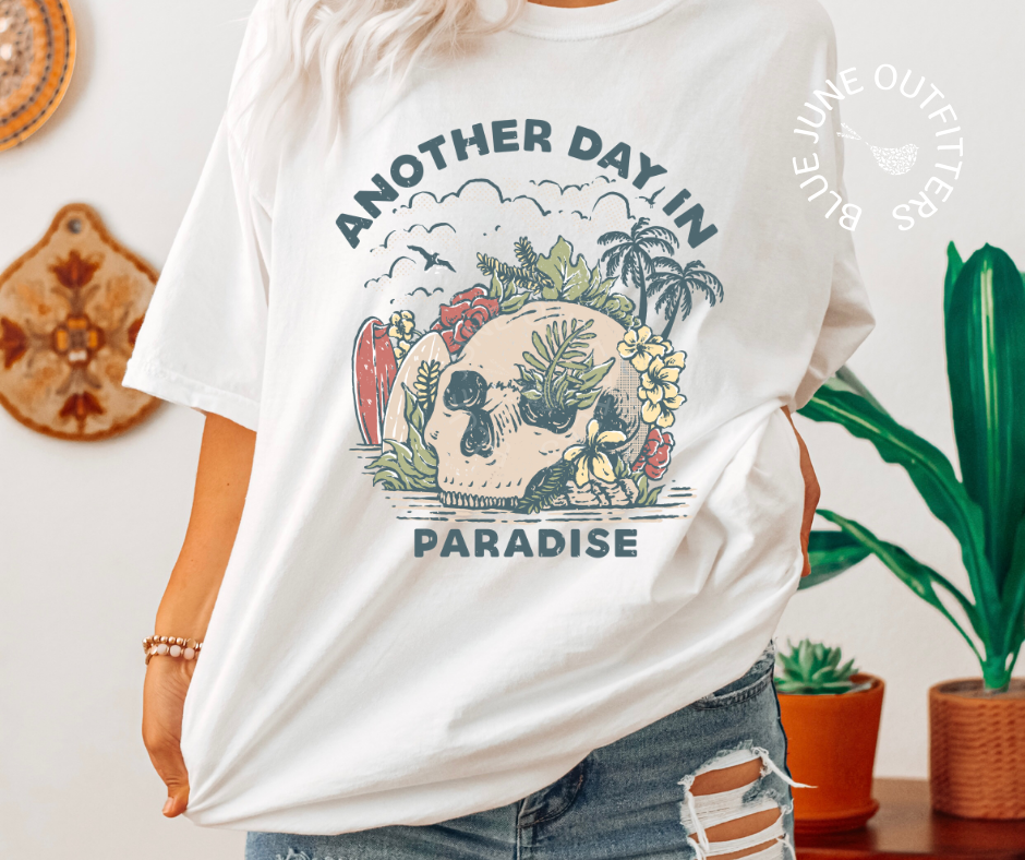 Female wearing the white t-shirt in size XL for an oversized look. This tee is features a skull on the beach with palm trees, surf boards and seagulls with the text another day in paradise. This is from Blue June Outfitters' exclusive Morbid Nature Collection.