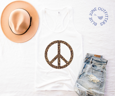 The white women's racerback tank top laid flat on a white surface. Shown here with a pair of jean shorts and trendy hat. The artwork is a leopard pattern peace sign.