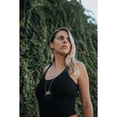 Female modeling the necklace. She is in nature wearing a black tank top and rust orange slacks. She has blonde hair and wearing long bohemian brass earrings.  She's wearing the raw citrine necklace. The pendant falls just below the diaphragm. 